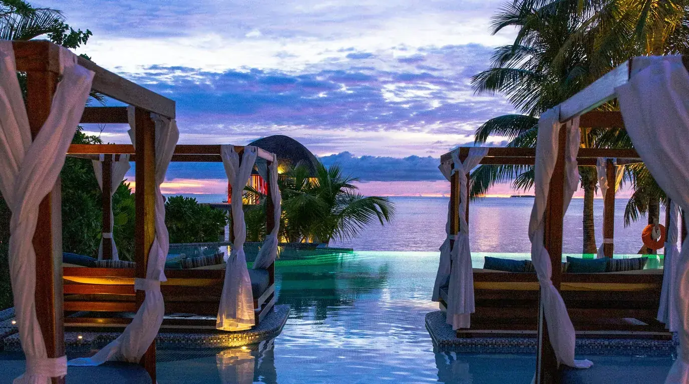 Curtained daybeds around an infinity pool looking out to the sea at dusk